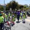 Students wearing yellow vests pause with their bikes by a table with staff during a school event.
