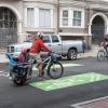 An adult and child ride a two-person bike on a bikeway that has green paint indicating bikes will be on the roadway.