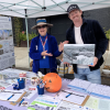 Two people looking at the camera while smiling and gesturing towards visual and printed information on a table