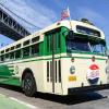 A vintage Muni bus that's green and cream in color passing under a bridge 