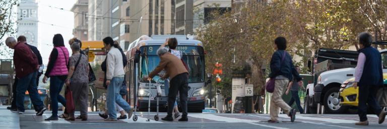 People walking across the Market Street in a crosswalk in front of a Muni bus