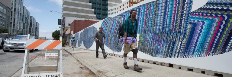 Two people walk by a mural consisting of overlapping circles of various colors