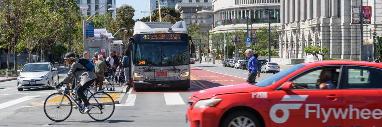 car, bike, pedestrian, taxi, bus and passengers on Van Ness Ave in Civic Center 