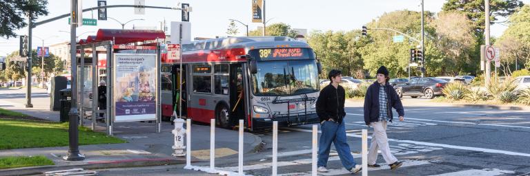 38R pulling away from bus stop on Geary. Two pedestrians crossing the street
