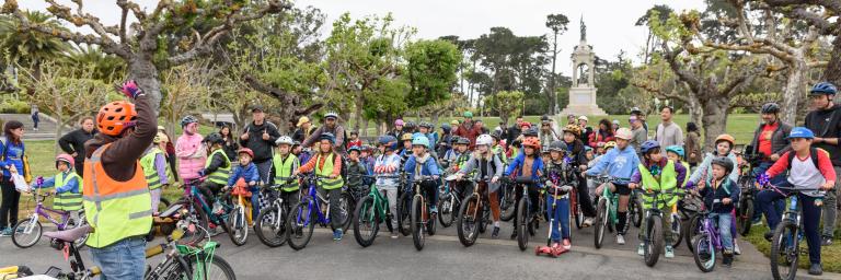 Kids and adults on bikes in front of trees.