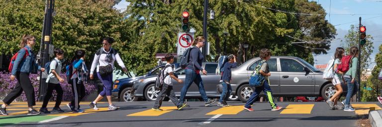 Children and teachers walk safely across an intersection in the cross walk as cars drive by