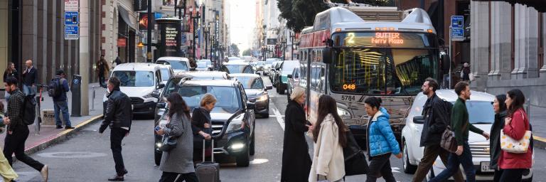 People walking on a crosswalk in front of traffic including a Muni bus