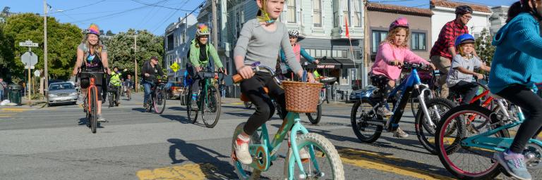 Students wearing helmets bike on a street for a school event.