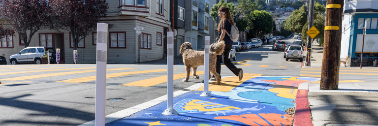 Painted corner on Sanchez street with person walking a dog in the crosswalk