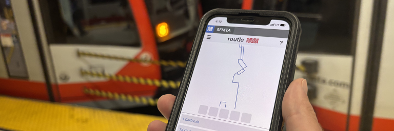 Hand holding smartphone with Routle on screen, train in the background