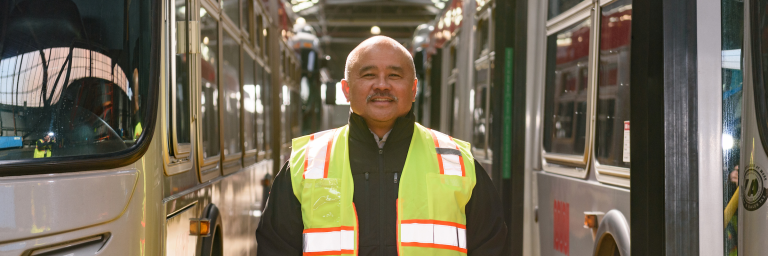 Muni Safe Driver Award Recipient Voltaire Barsana standing between two buses