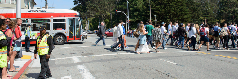 People crossing street heading to Golden Gate Park with a 29 Bus and Muni Staff