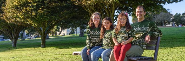 Family sitting on a park bench wearing the 2026 Muni Holiday Sweater