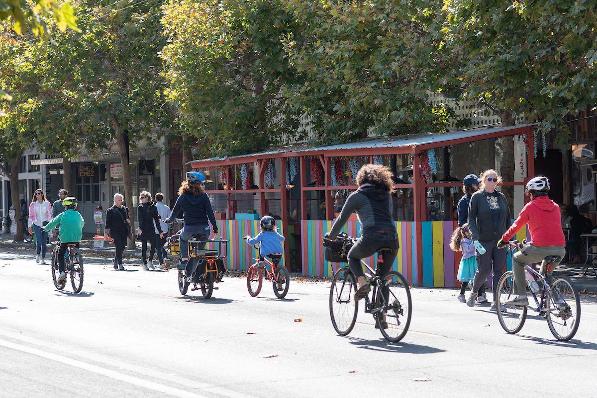 Adults and kids bike on Valencia Street near a colorful parklet. Adults and kids bike on Valencia Street near a colorful parklet.