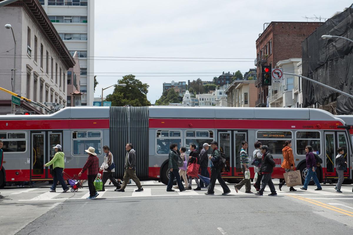 People cross the street as a bus passes them in the background in the same intersection. People cross the street as a bus passes them in the background in the same intersection.