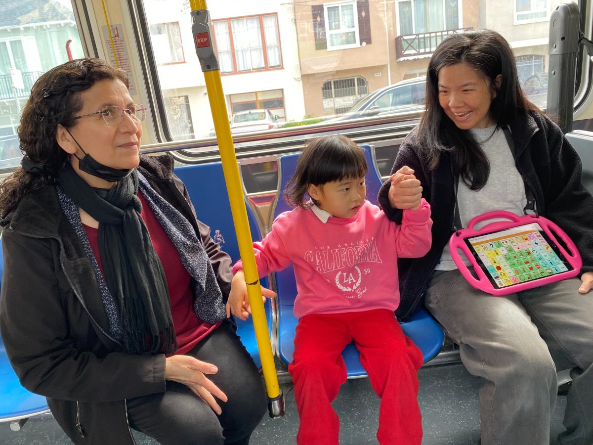 A young child holds hands with two adults on a bus. A young child holds hands with two adults on a bus.