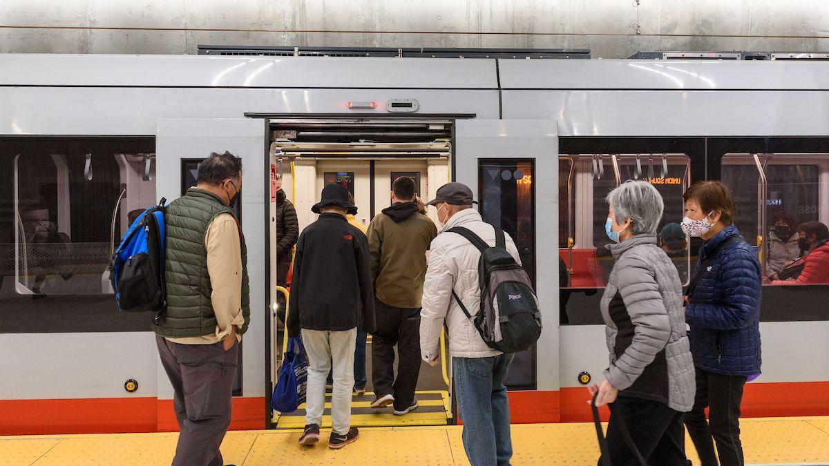 Several people board a Muni train from a station platform. 