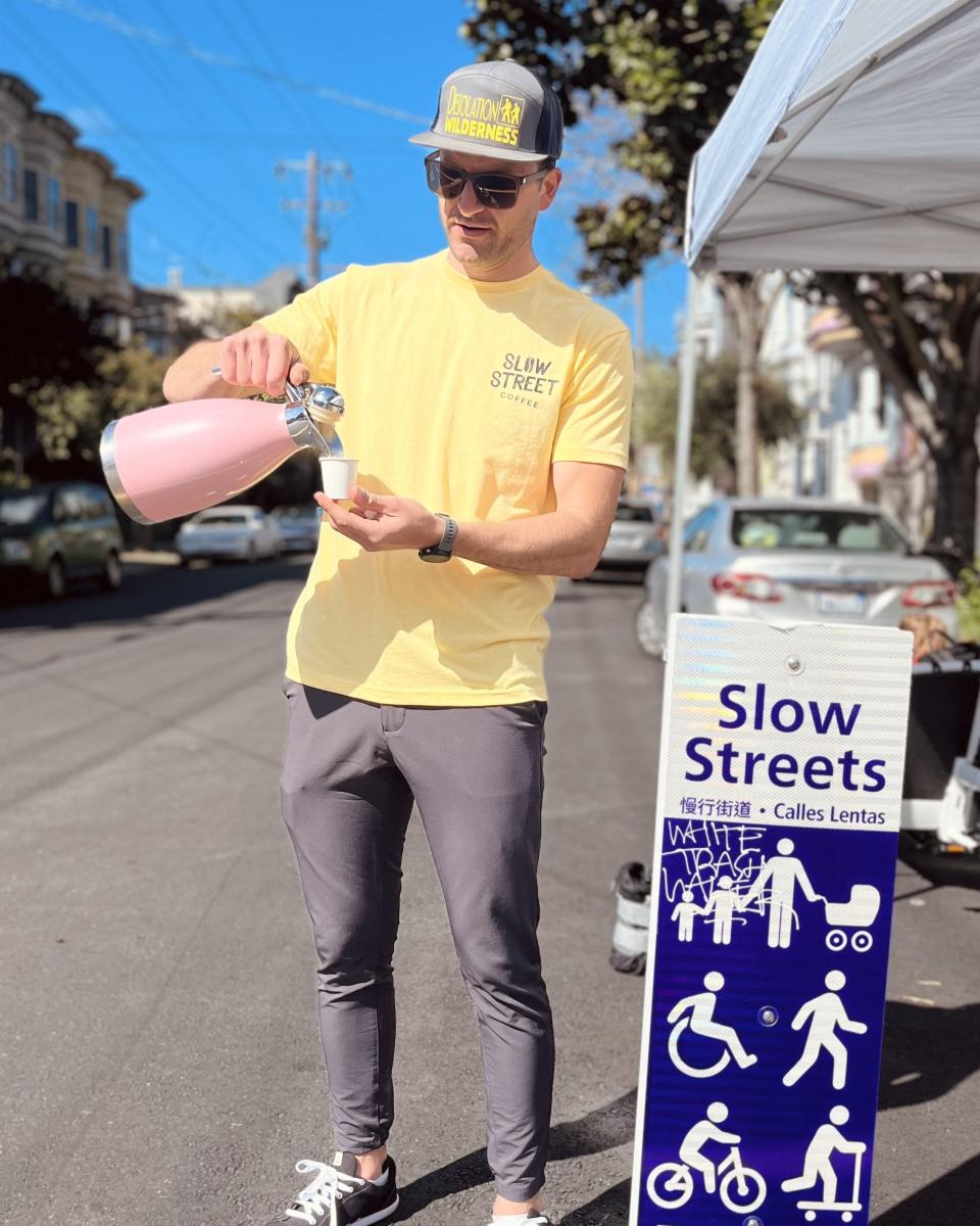 A man in a yellow shirt pouring a drink into a cup.