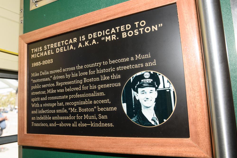 A framed plaque installed inside a vintage streetcar. It features a photo of Mike Delia in a vintage uniform and text honoring his life and work with Muni.