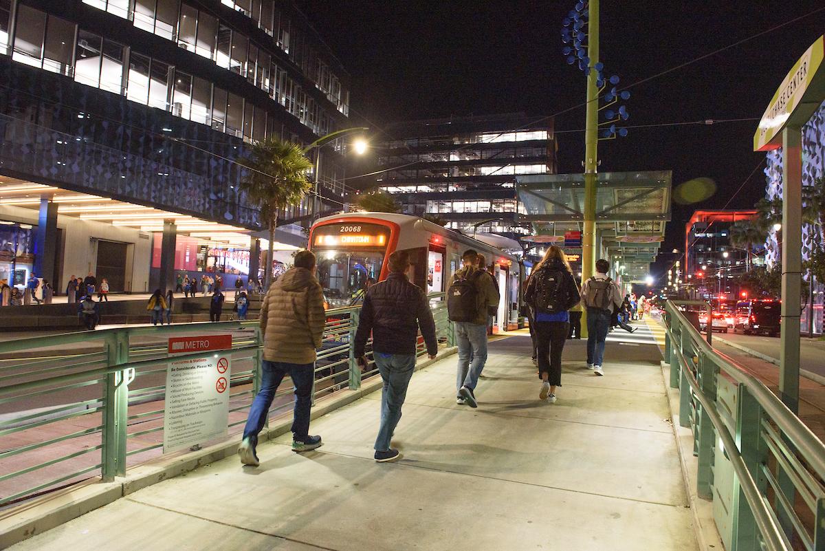 Several people walk up a ramp toward a T Third train that's waiting at a platform near Chase Center in the evening.
