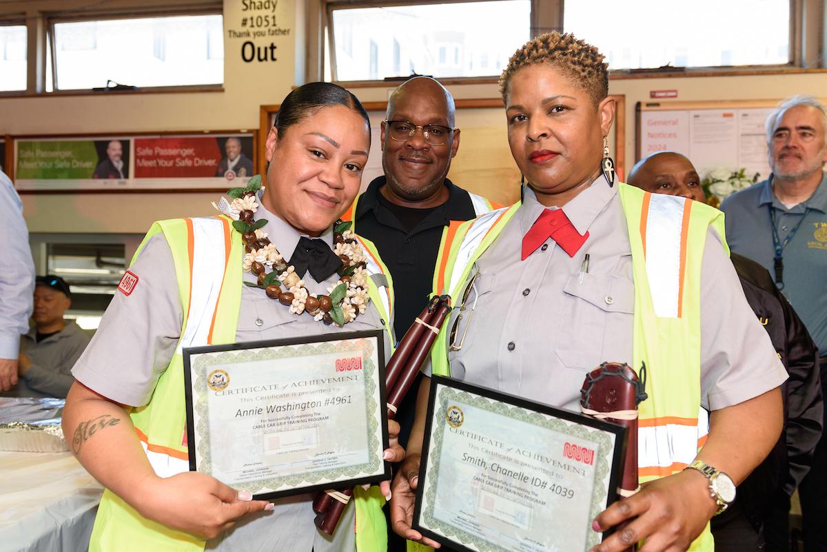 A photo of Annie Washington and Chanelle Smith, two of Muni’s newest cable car grips, holding up certificates of achievement.