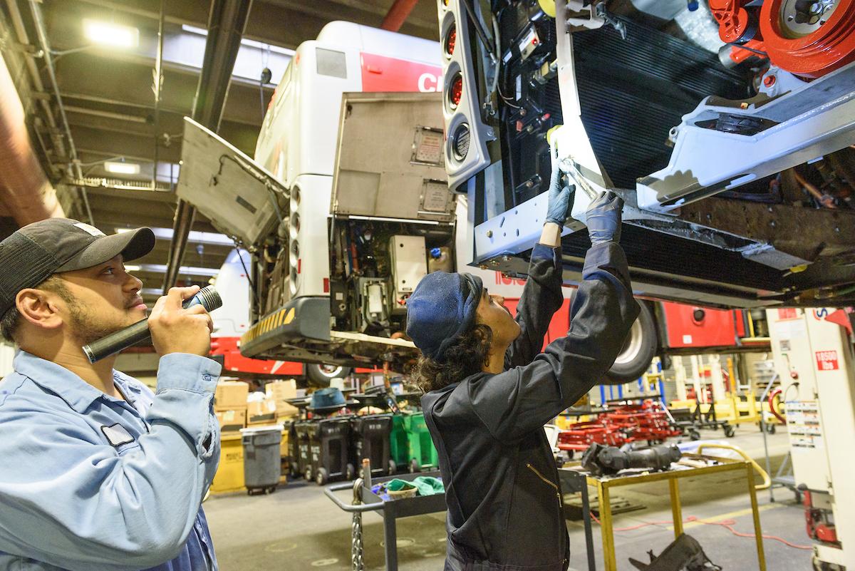Two people inspect part of a Muni bus in one of the SFMTA's shops.