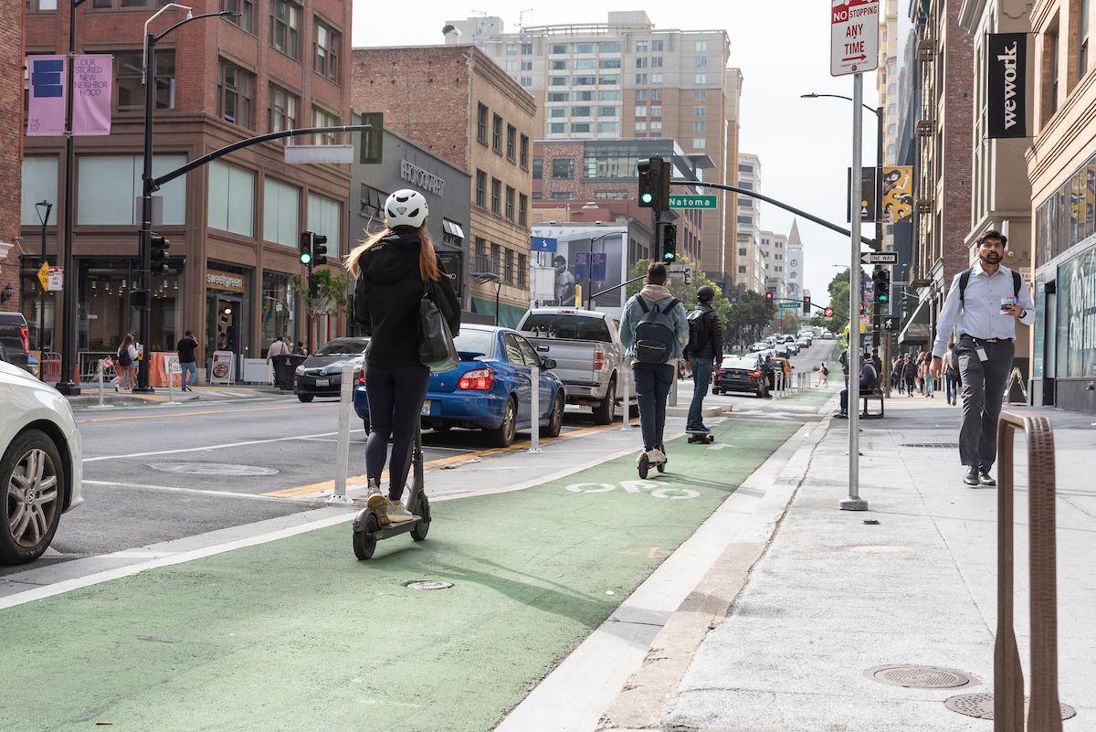 Three people riding scooters use a green bikeway in the downtown area. 