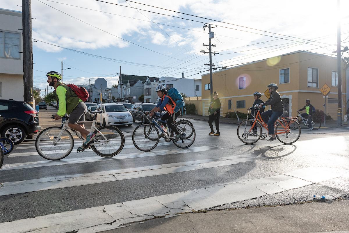 Several people bike across an intersection in a residential area.