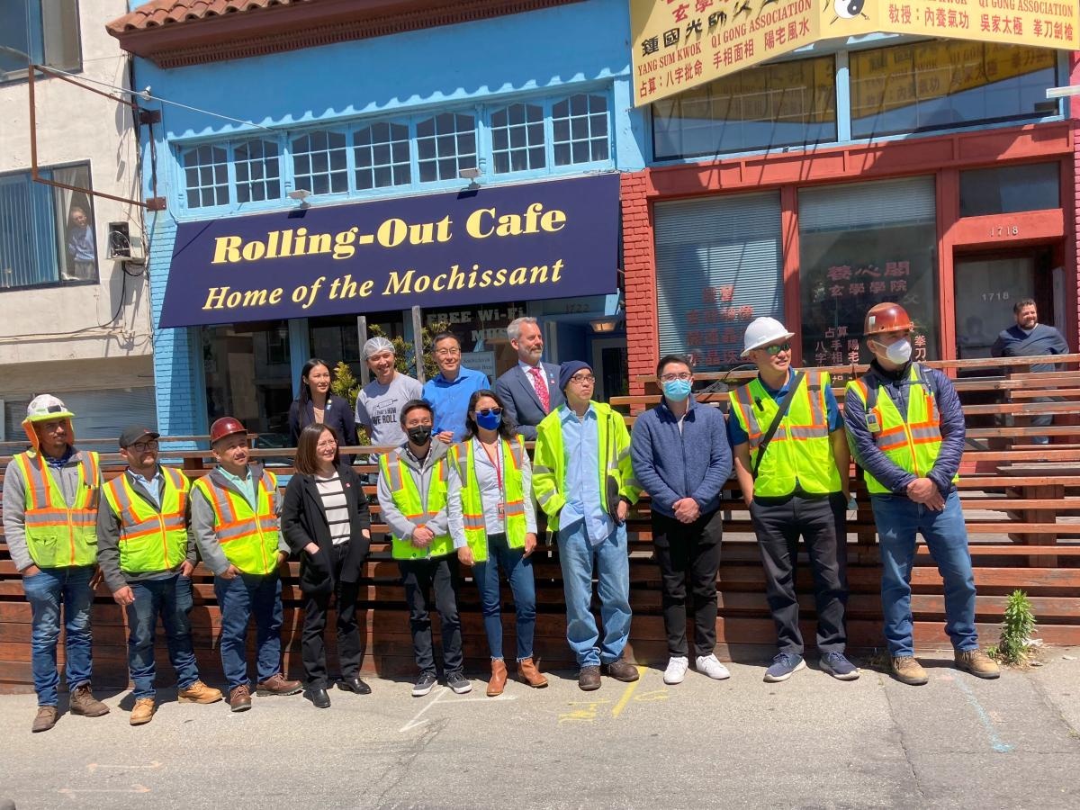 Several people wearing safety vests stand together, posing for a photo in front of Rolling-Out Cafe.