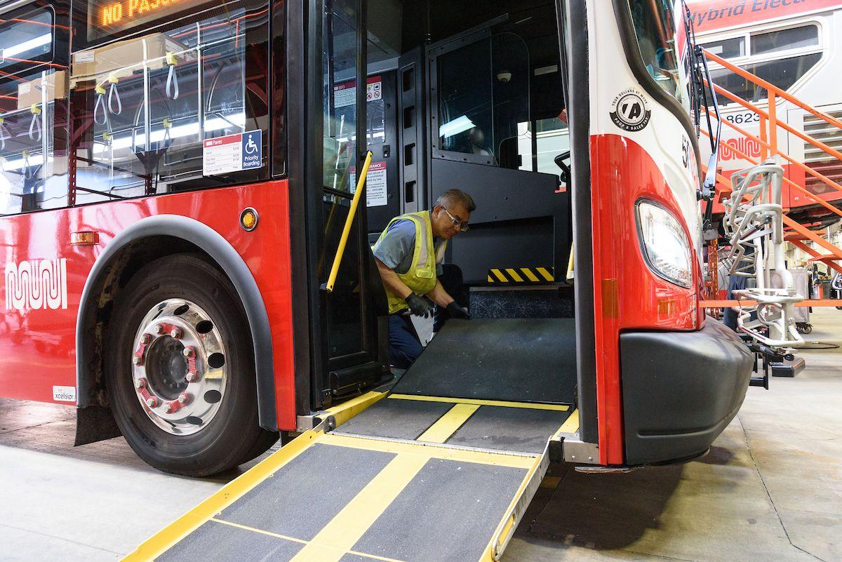 Close-up photo of an SFMTA staff member inside a bus inspecting a wheelchair accessible bus ramp.