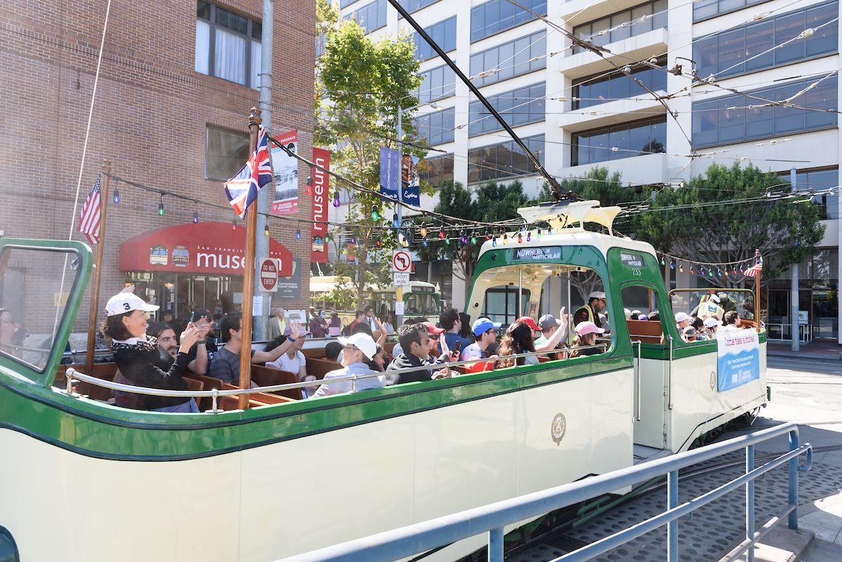Photo shows a boat tram historic streetcar full of people, with some taking pictures of the vehicle.