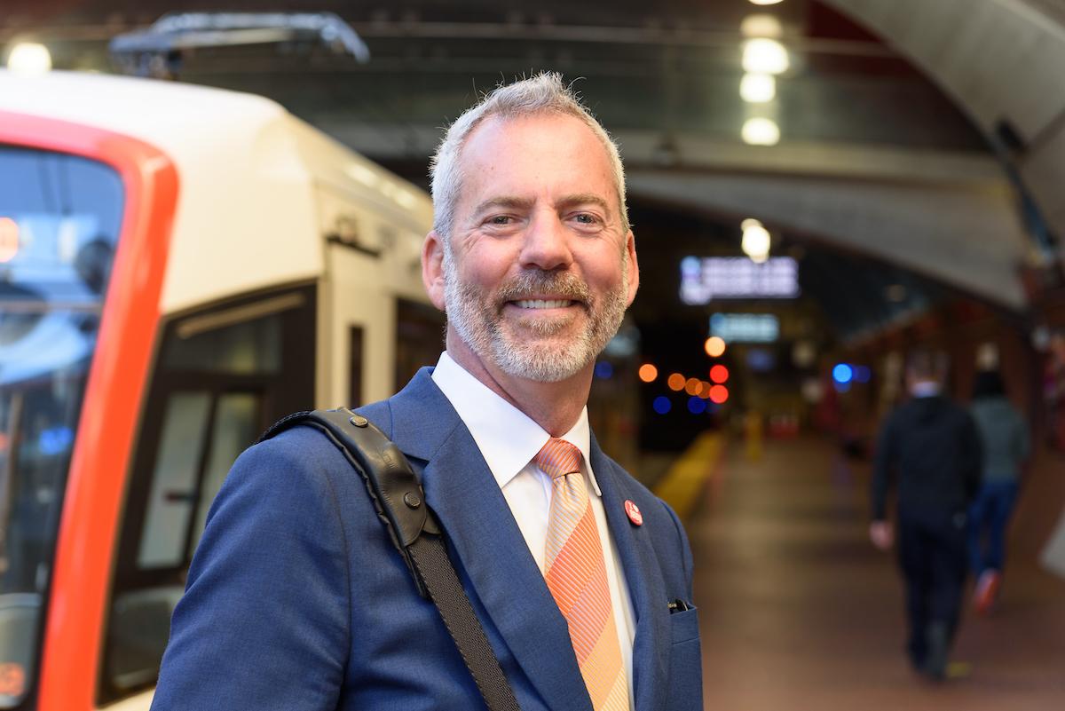 Jeff Tumlin stands on the West Portal Station platform as a train stops nearby.