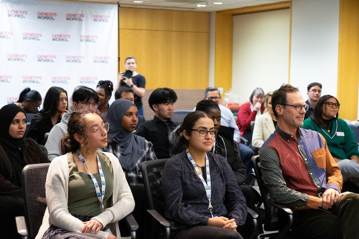 Genesys interns and their managers listen to a presentation in a conference room.