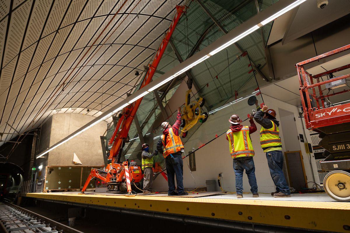Crews install glass for the Chinatown-Rose Pak Station escalators at the platform level.