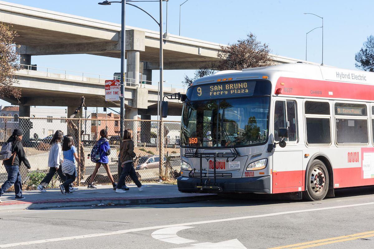 Several young people walk toward a 9 San Bruno Muni bus to board.