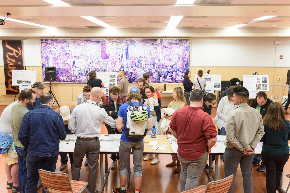 Several people stand around a table to review bikeway designs during a public event about the Valencia Bikeway Improvements project.