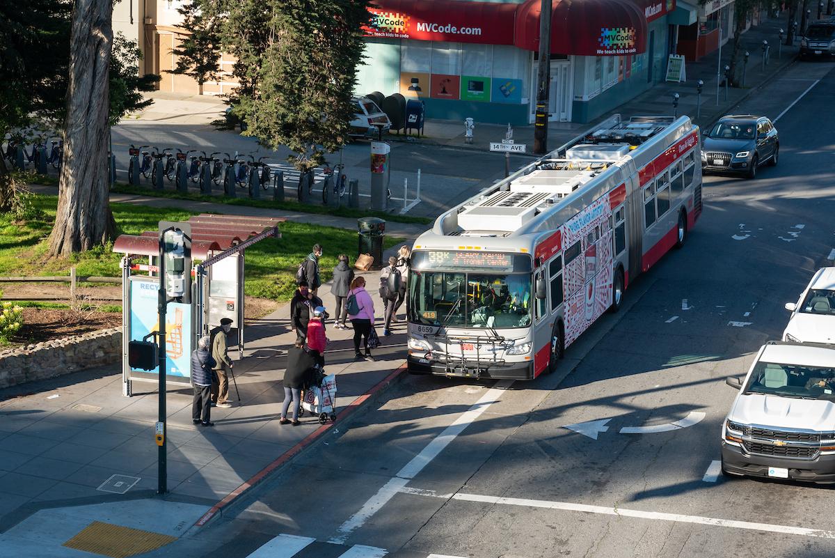 People boarding a bus with cars nearby.