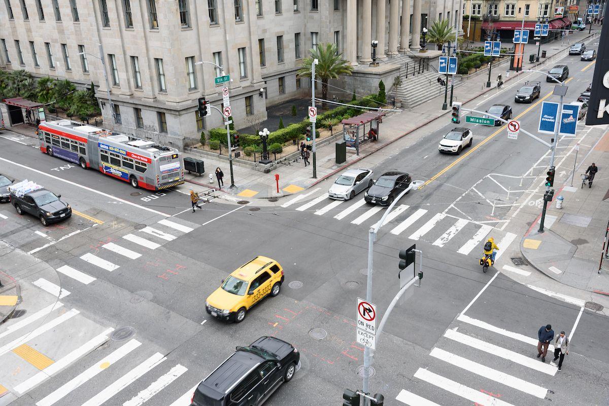Aerial view of a downtown intersection. Cabs, cars and bikes pass through.