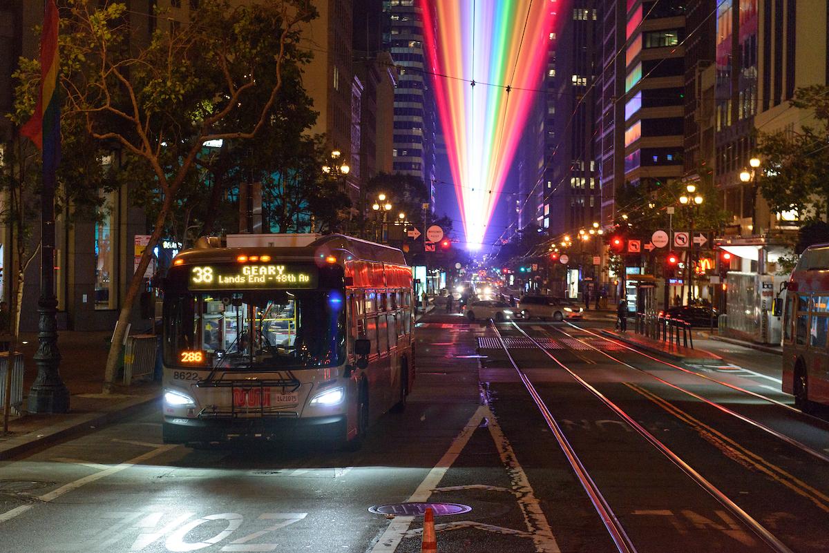 A bus on the street with rainbow lights above.