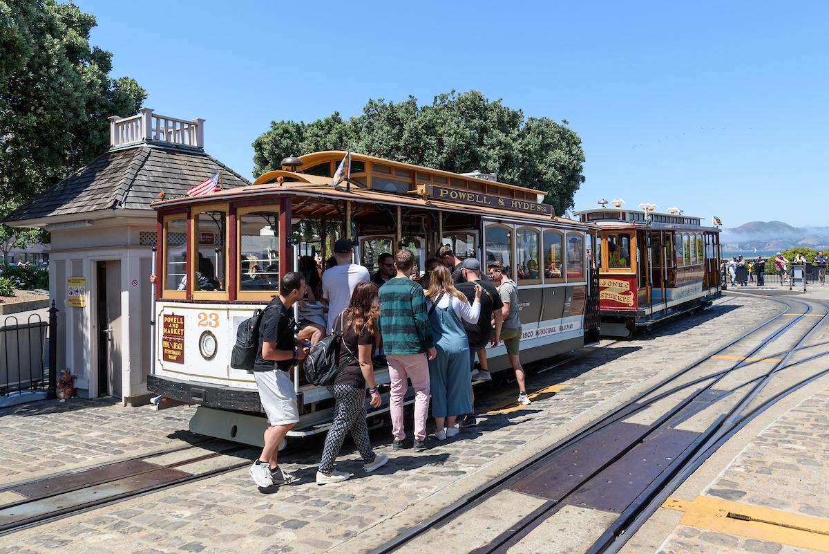 People board a cable car with views of the North Bay in the background.