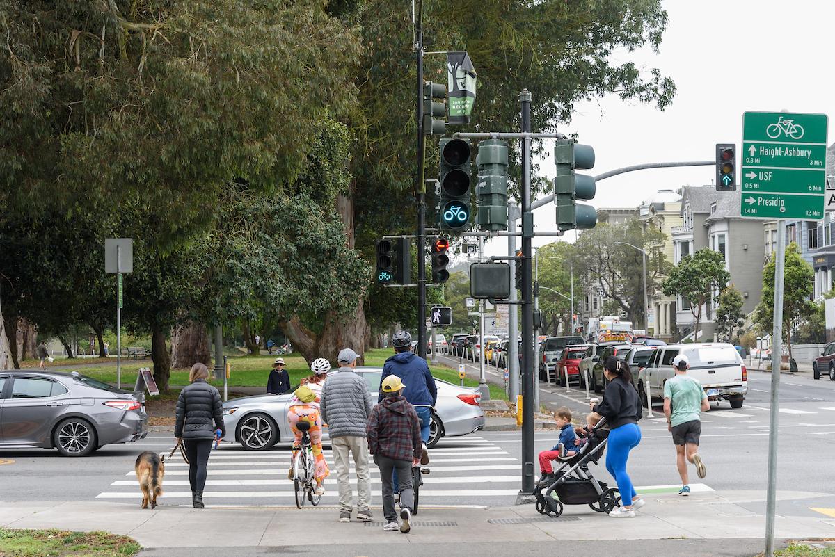 People walk, bike and push strollers across an intersection in the Panhandle.