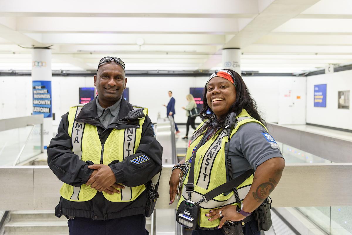 Two transit fare inspectors wear yellow safety vests as the stand in a Muni Metro station.