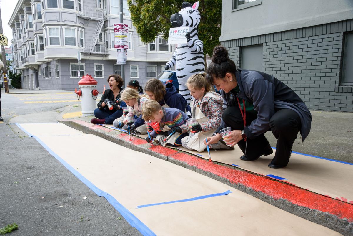 SFMTA Streets Director Viktoriya Wise and several children paint a curb red for our new daylighting program.