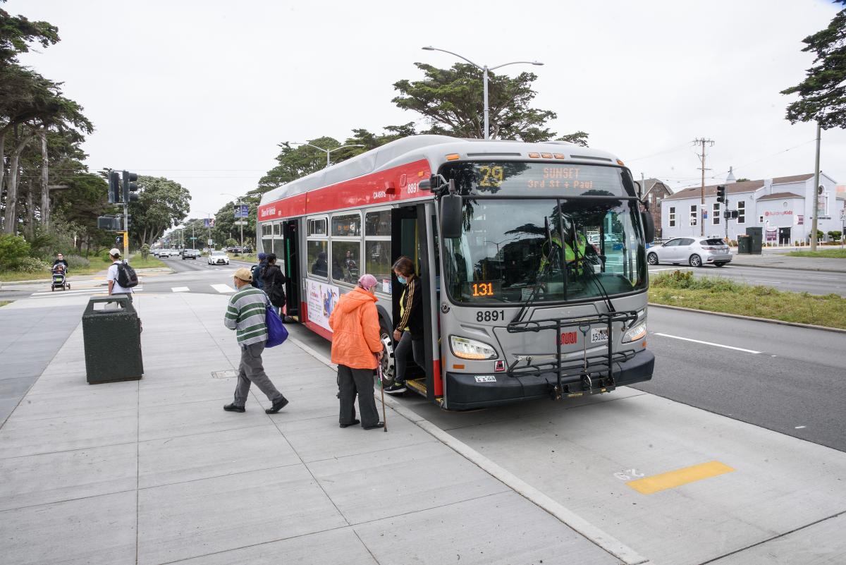 A 29 Sunset bus stops, and a person with a cane waits to board as riders step off the bus.