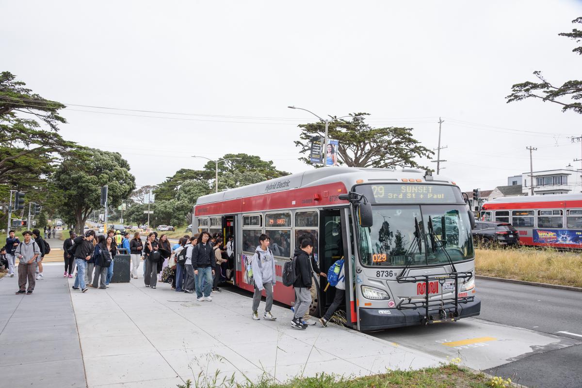 Many students board a 29 Sunset at an upgraded stop that features pavement running the length of the bus.