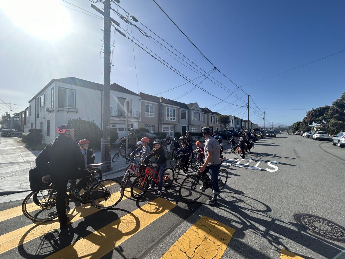 Kids and adults on bikes in the street in front of homes.
