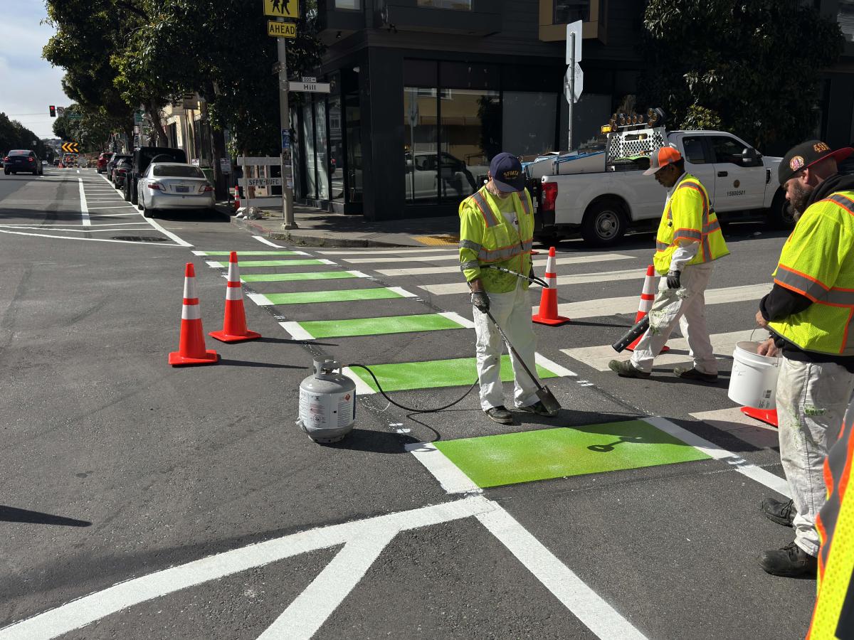 Crews wearing yellow safety vests paint part of Valencia Street green and white to mark the new side-running bikeway.