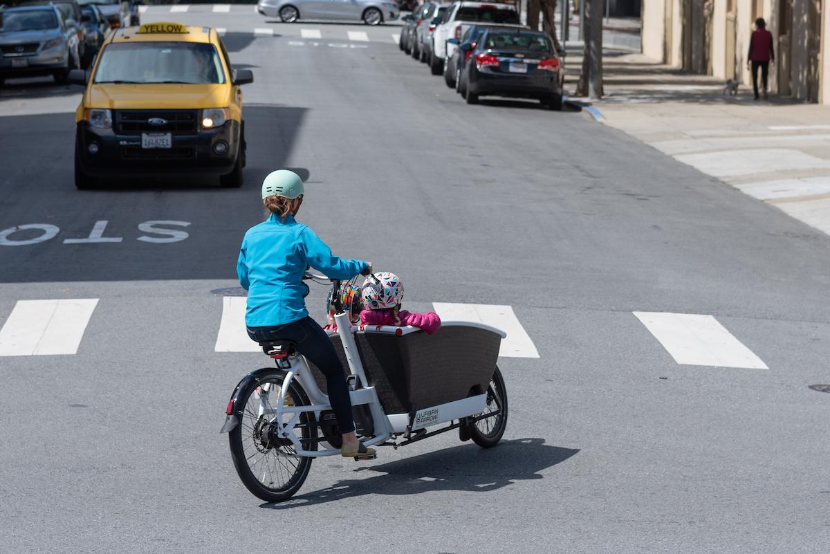 Woman rides a bike with two children in a front seating area of the bike.