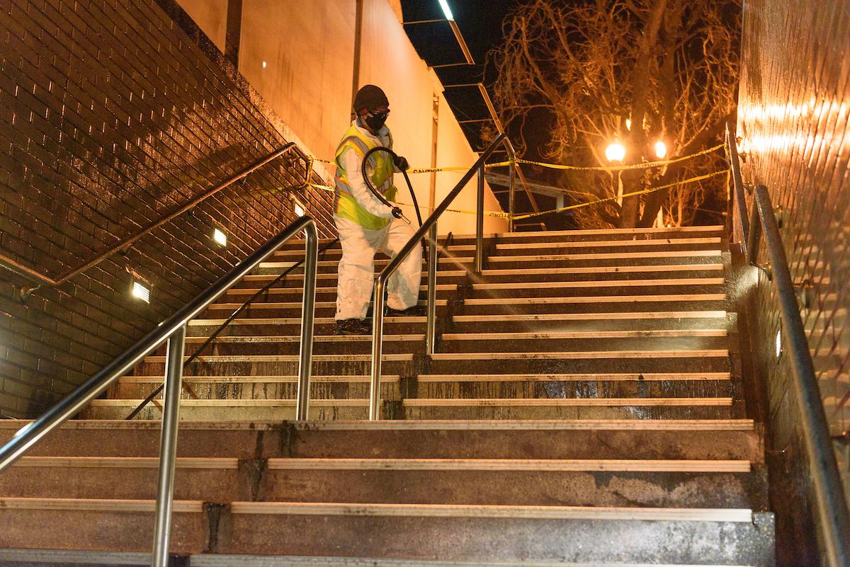 Custodian uses a hose to clean stairs at a Muni station during an evening shift.