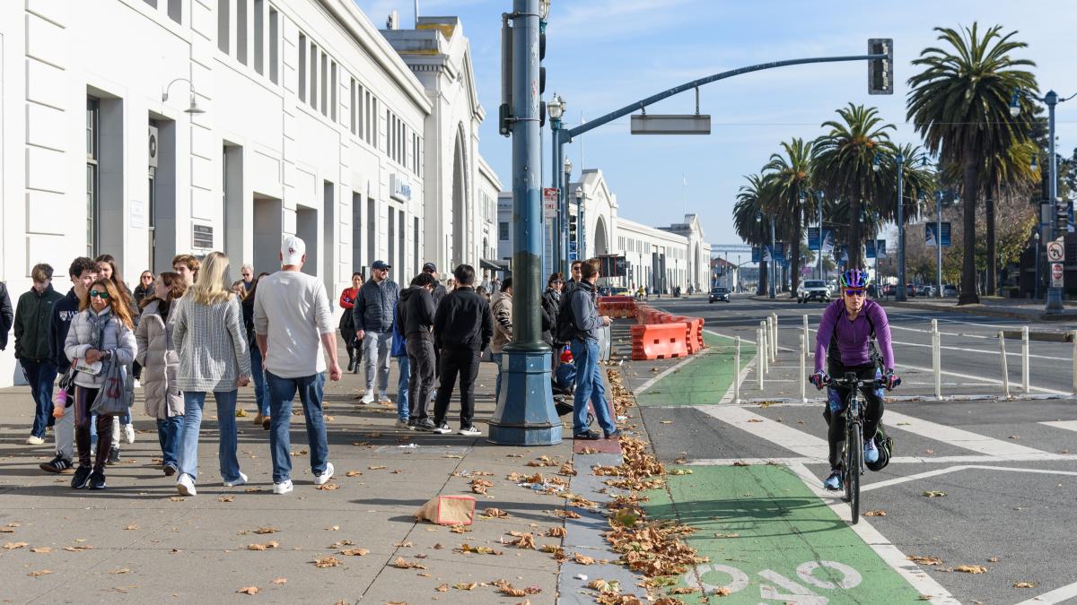 A person bikes in a protected green bikeway near a crowd of people walking on a sidewalk.